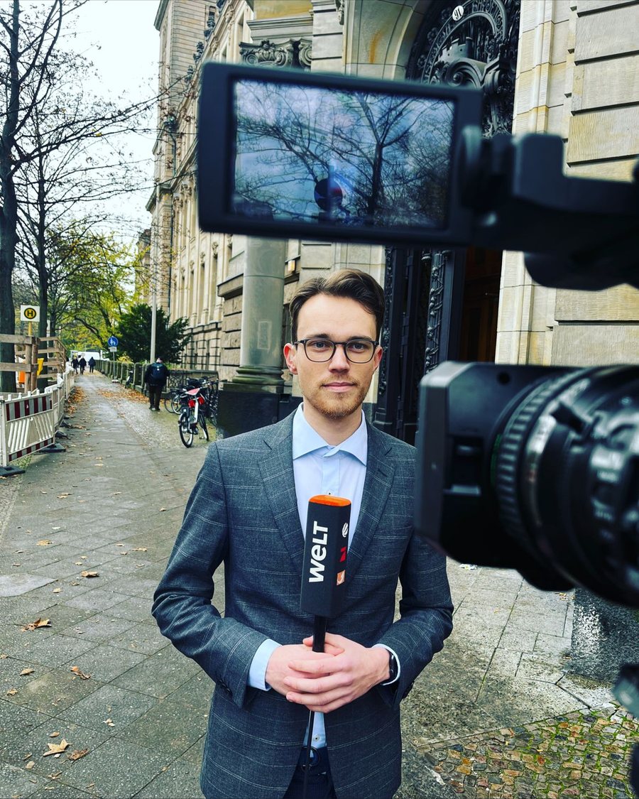 Paul Klinzing als Reporter mit Mikrofon vor einer Fernsehkamera in Berlin